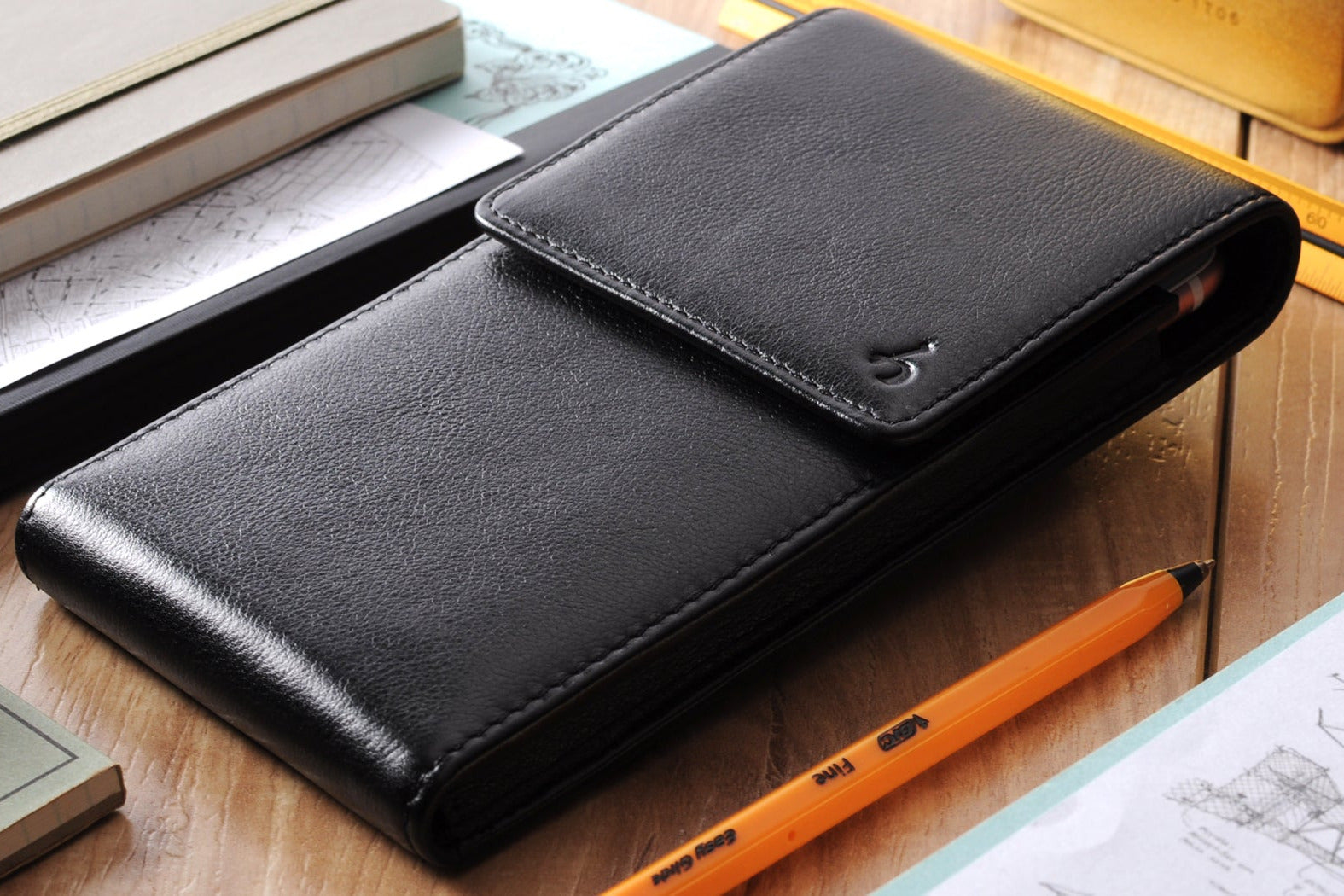 Black leather wallet on a wooden surface with an orange pen and books in the background